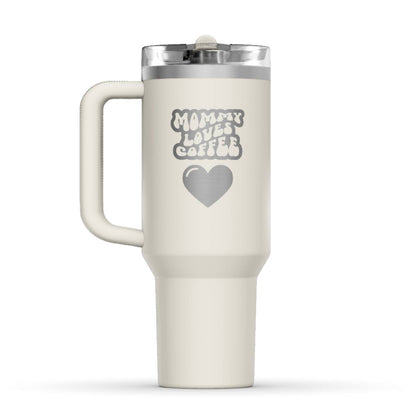 Stanley 40oz Tumbler, with a personalized twist. The perfect gift for mom. The Color of the cup is Cream, a shade of off-white. It’s engraved with a typically 70s retro-style font, saying Mommy Loves Coffee. Under that text there is a nice big heart in the same style. 