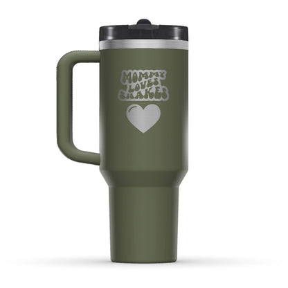 The back side of the newest Stanley 40oz Tumbler. The perfect gift for mom. The Color of the cup is Dried Pine, a dark shade of army green. It’s engraved with a typically 70s retro-style font, saying Mommy Loves Shakes. Under that text there is a nice big heart in the same retro style.