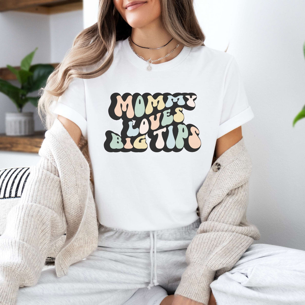 Graphic tee for women. The color of the shirt is white. In a colorful, typically 70s retro-style font it says Mommy Loves Big Tips.