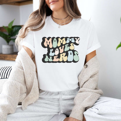 Graphic tee for women. The color of the shirt is white. In a colorful, typically 70s retro-style font it says Mommy Loves Nerds.