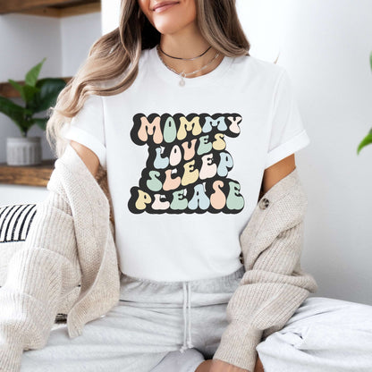 Graphic tee for women. The color of the shirt is white. In a colorful, typically 70s retro-style font it says Mommy Loves Sleep Please.