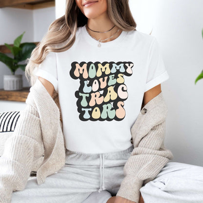 Graphic tee for women. The color of the shirt is white. In a colorful, typically 70s retro-style font it says Mommy Loves Tractors.