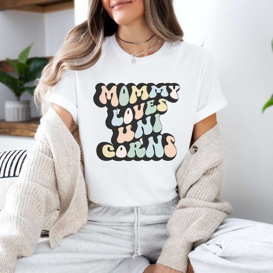 Graphic tee for women. The color of the shirt is white. In a colorful, typically 70s retro-style font it says Mommy Loves Unicorns.